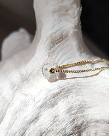 Gold memorial necklace with a clear pendant on a white marble surface.