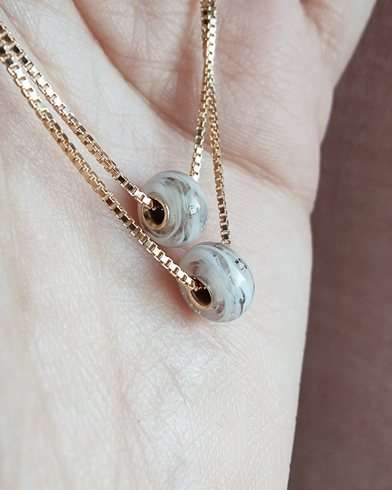 Gold memorial necklace with two gray beads on a light skin background.