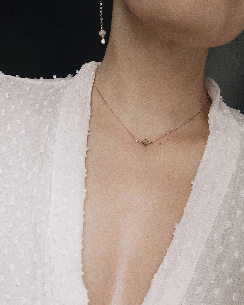 Close-up of a person wearing a delicate memorial necklace with a small memorial pendant, against a neutral background.