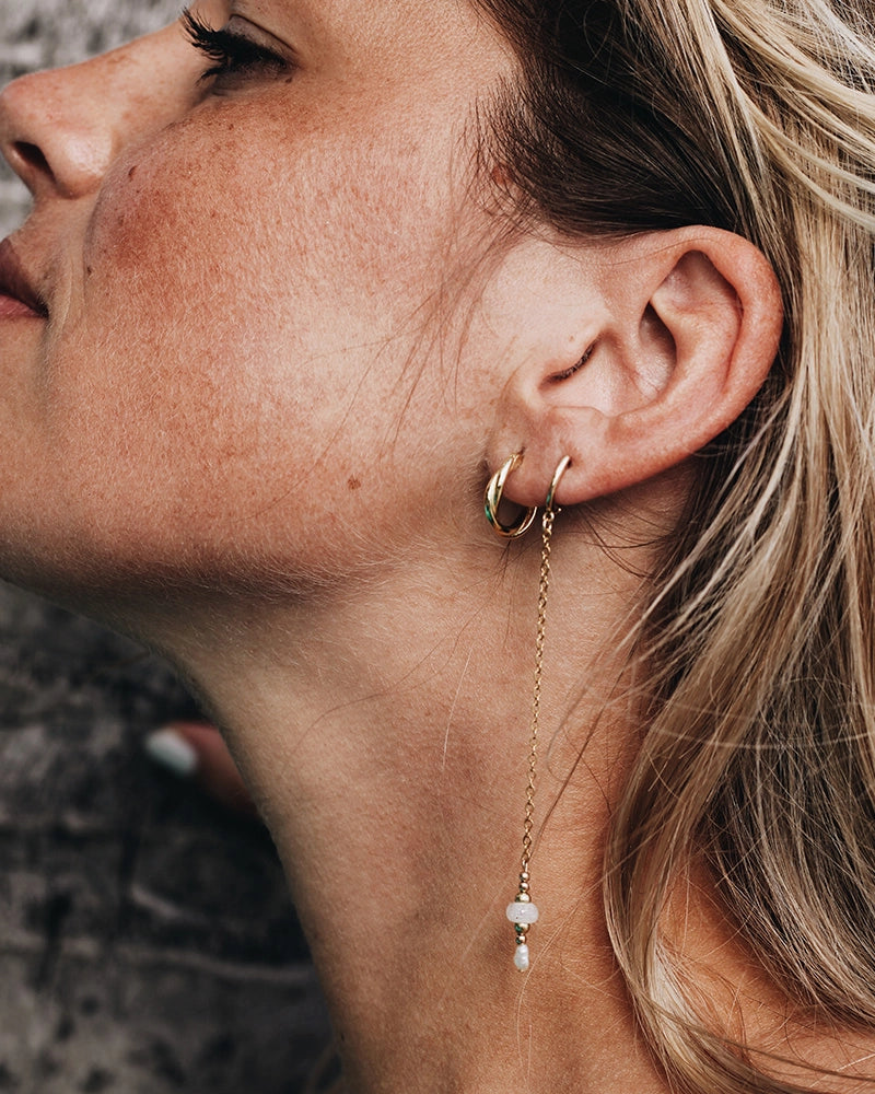 Close-up of a woman wearing gold cremation earrings with a dangling chain and beads.
