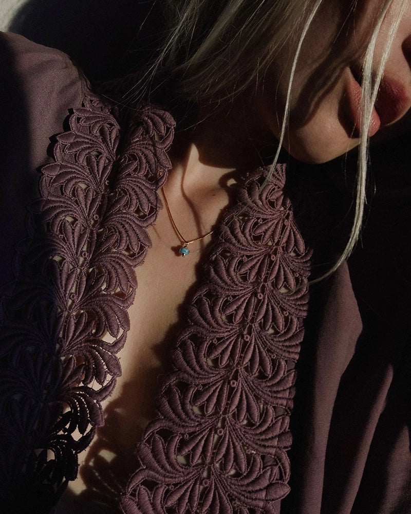 Close-up of a person wearing a memorial necklace and dark purple embroidered garment with a blurred background.