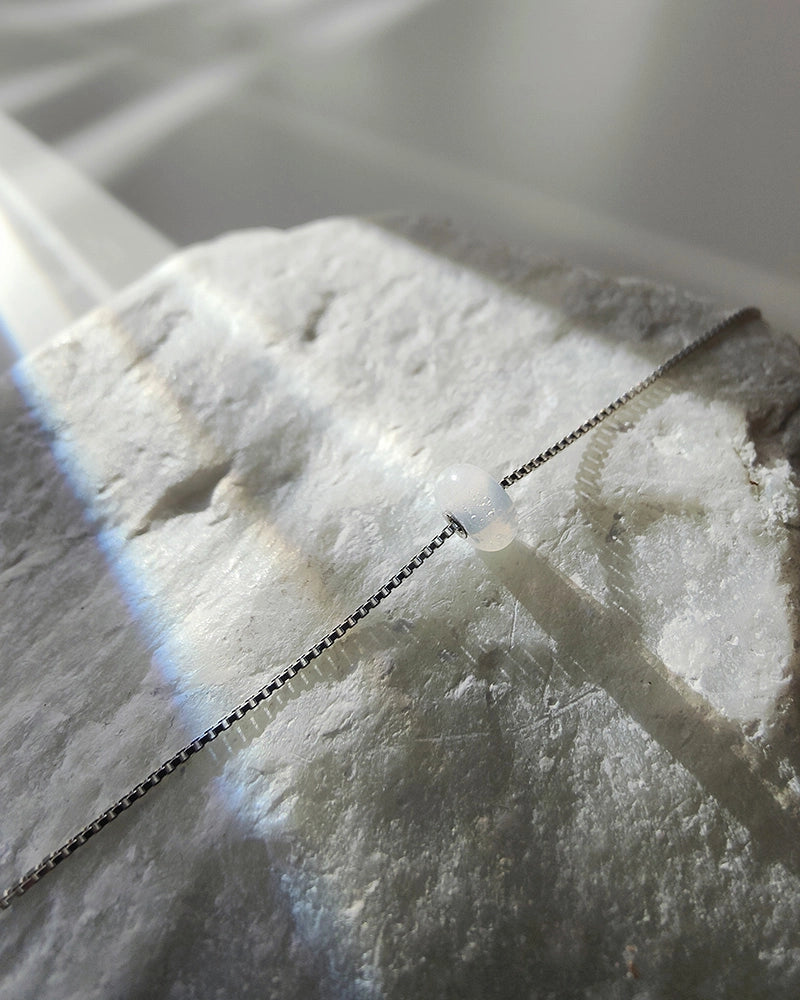 Close-up of a white ceramic tile with a memorial necklace draped over it.