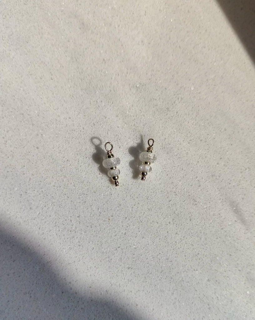 Pair of double memorial earrings and pendants with clear beads on a light gray background.