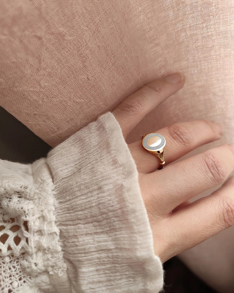 Close-up of a hand wearing a gold memorial ring with a white stone on a beige background.