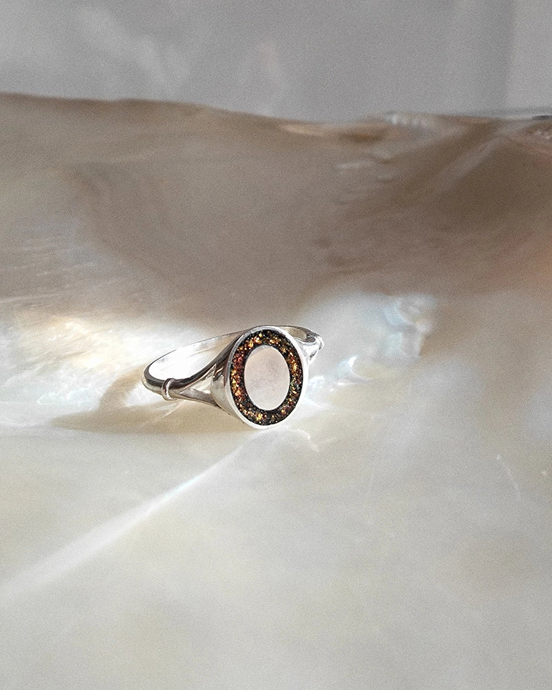 Silver memorial ring with a circular design on a shell background with ashes and hair encased of a lost loved one.