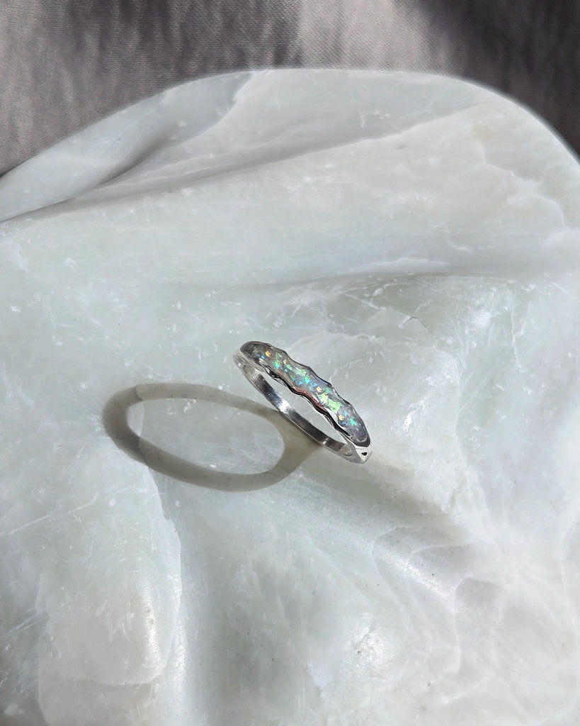 Silver memorial cremation ring with opal stones on a white fabric background.