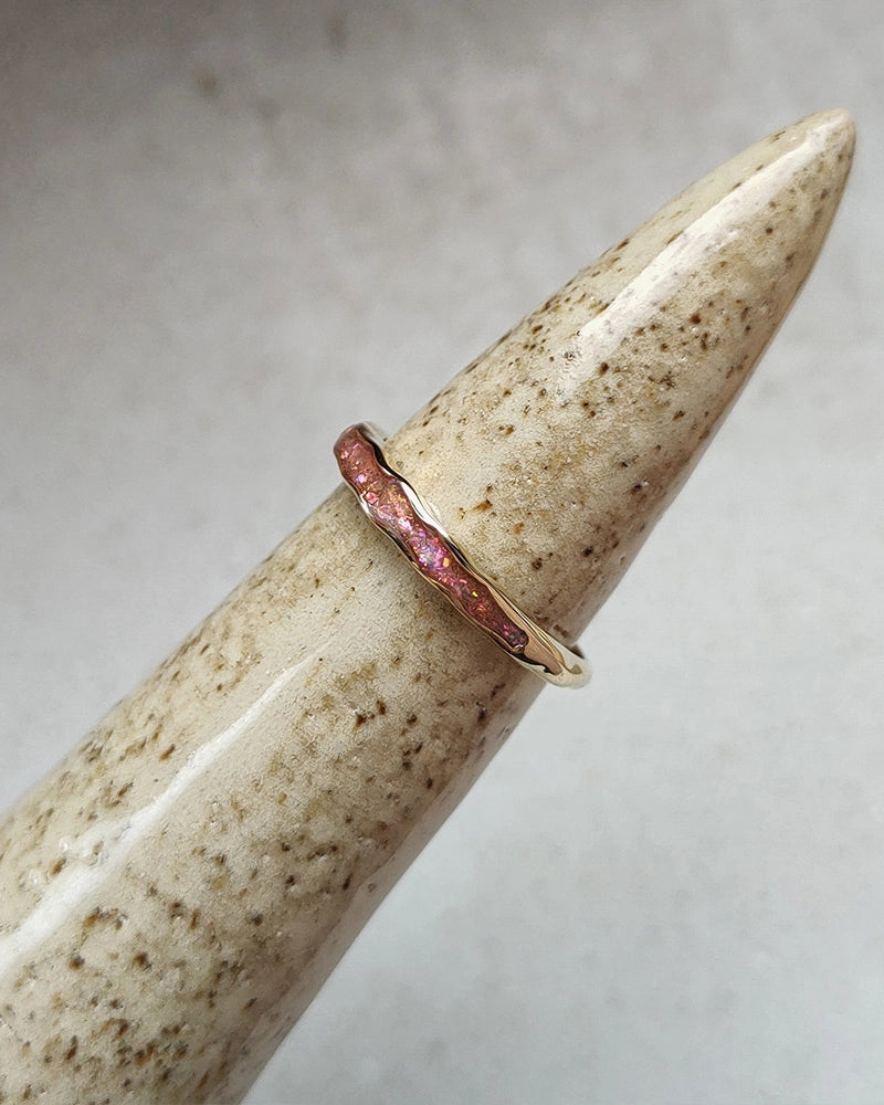 Rose gold memorial ring on a textured beige surface with a neutral background.