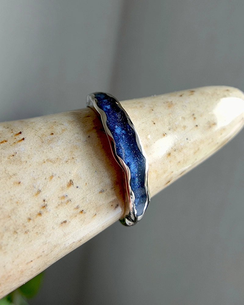 Silver memorial ring with blue stone on a beige stone surface.