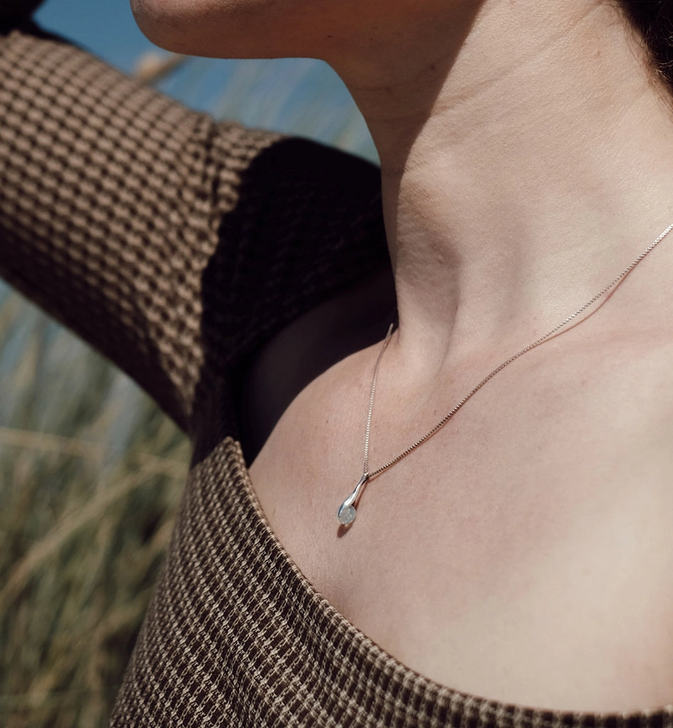 Person wearing a delicate memorial necklace with a blurred natural background.