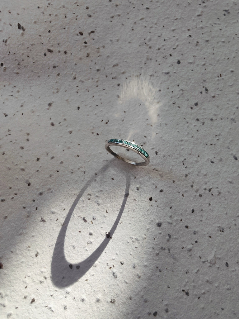 Silver memorial cremation ring with greenstone on a textured surface.