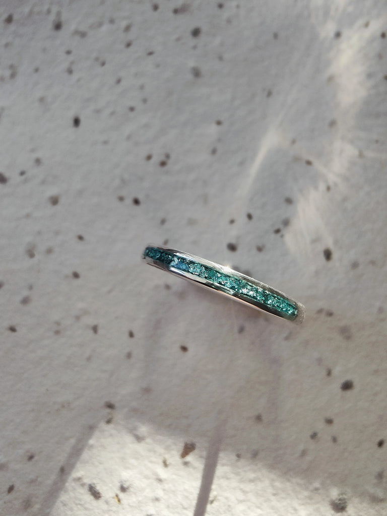 Memorial ring with green gemstones on a textured white background.