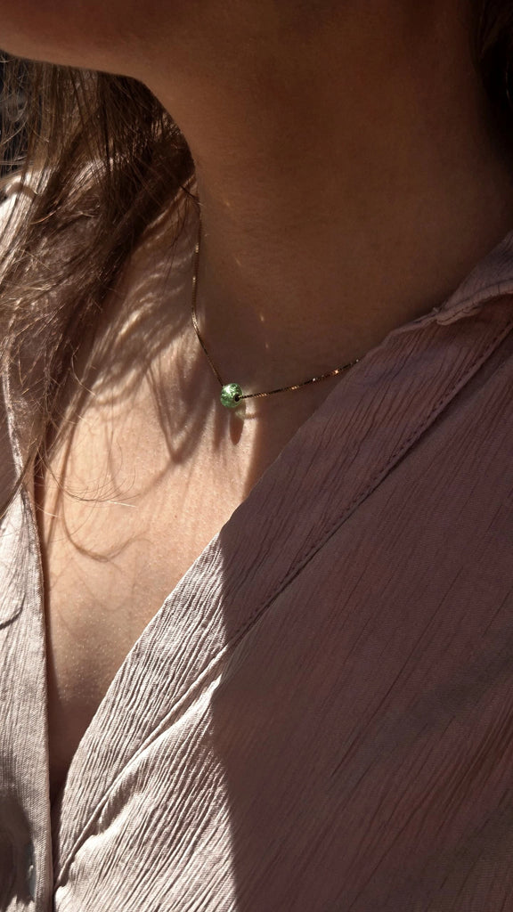 Close-up of a person wearing a delicate memorial remembrance necklace with a green gemstone.