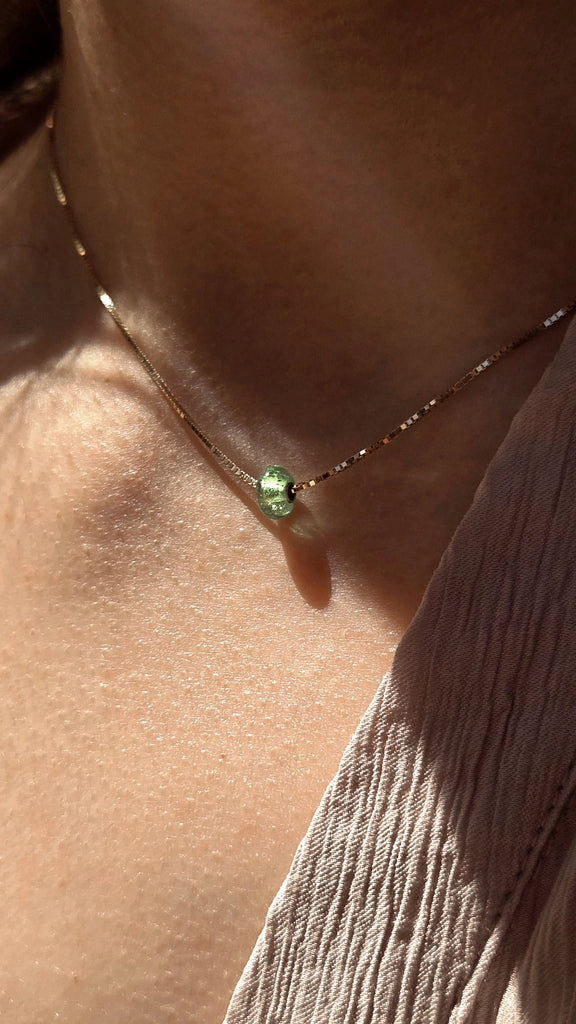 Memorial necklace with a green gemstone worn by a person to remember a lost loved one.