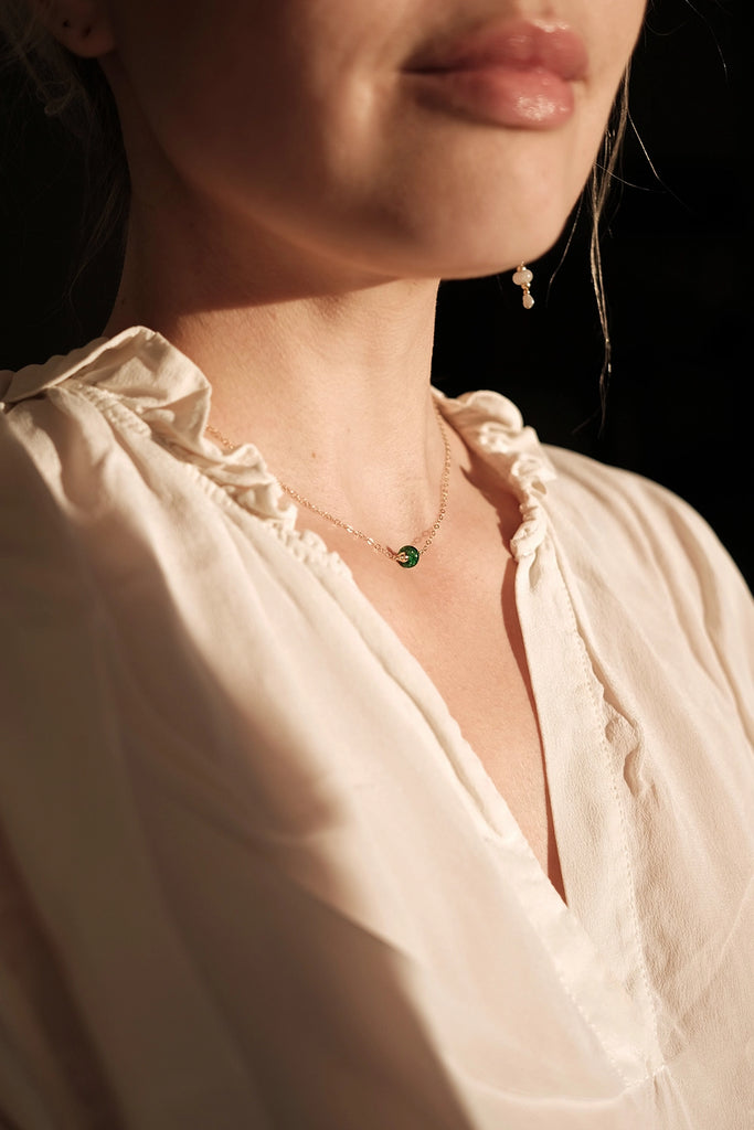 Close-up of a person wearing a delicate memorial necklace with a green pendant against a dark background to remember a lost loved one.