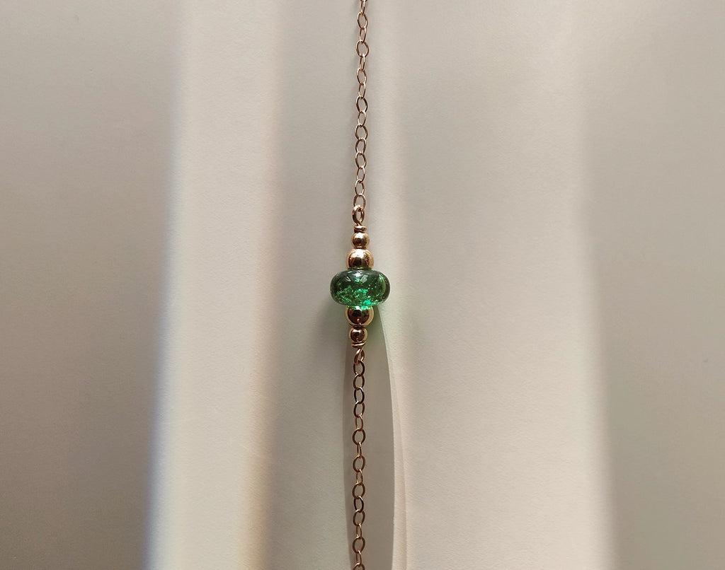 Memorial necklace with a green bead with ashes encased on a plain background.