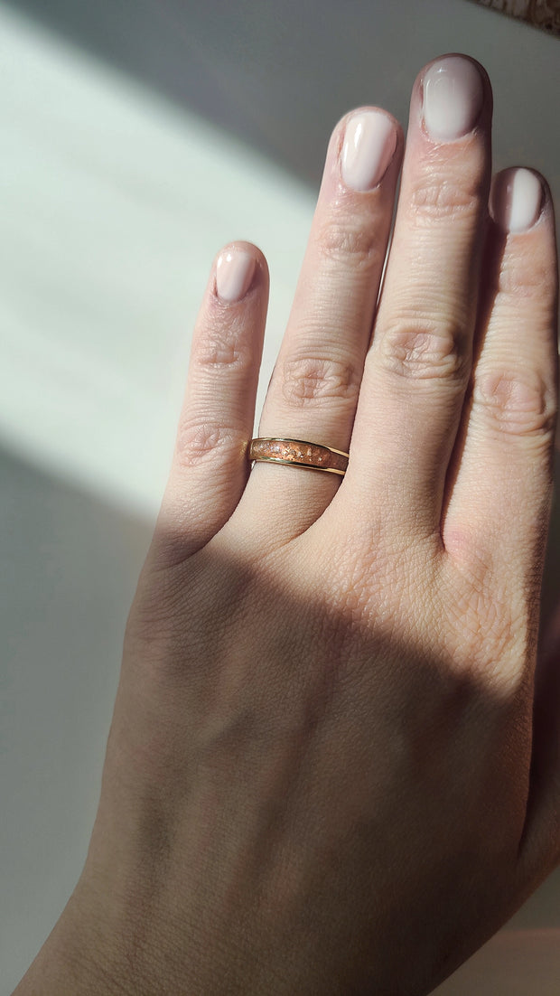 Hand wearing a gold cremationring with a neutral background.