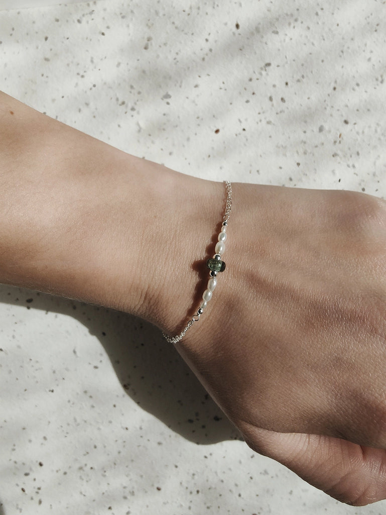 Close-up of a wrist wearing a delicate memorial bracelet with white pearls on a textured surface.