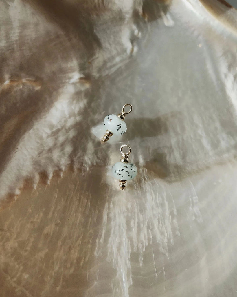 Pair of memorial pendants with blue beads on a textured beige surface.