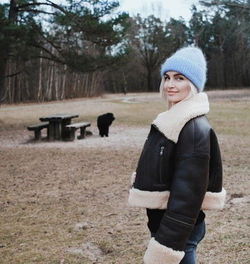 Linda Visser wearing a black jacket with white fur trim and a blue beanie standing in a park.