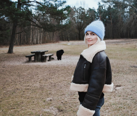 Linda Visser wearing a black jacket with white fur trim and a blue beanie standing in a park.