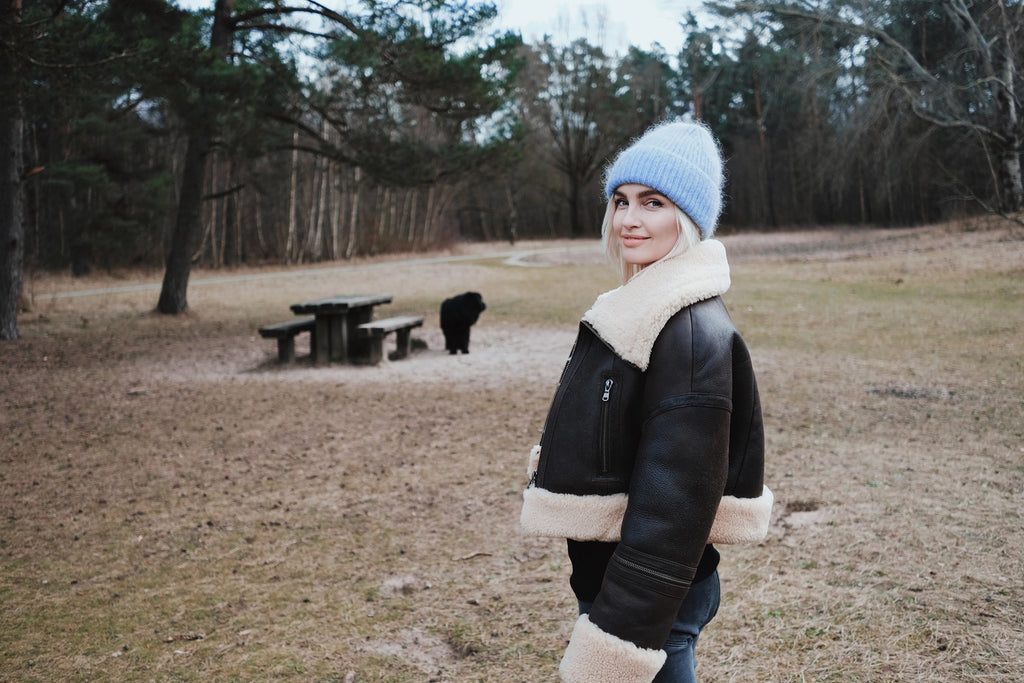 Linda Visser wearing a black jacket with white fur trim and a blue beanie standing in a park.