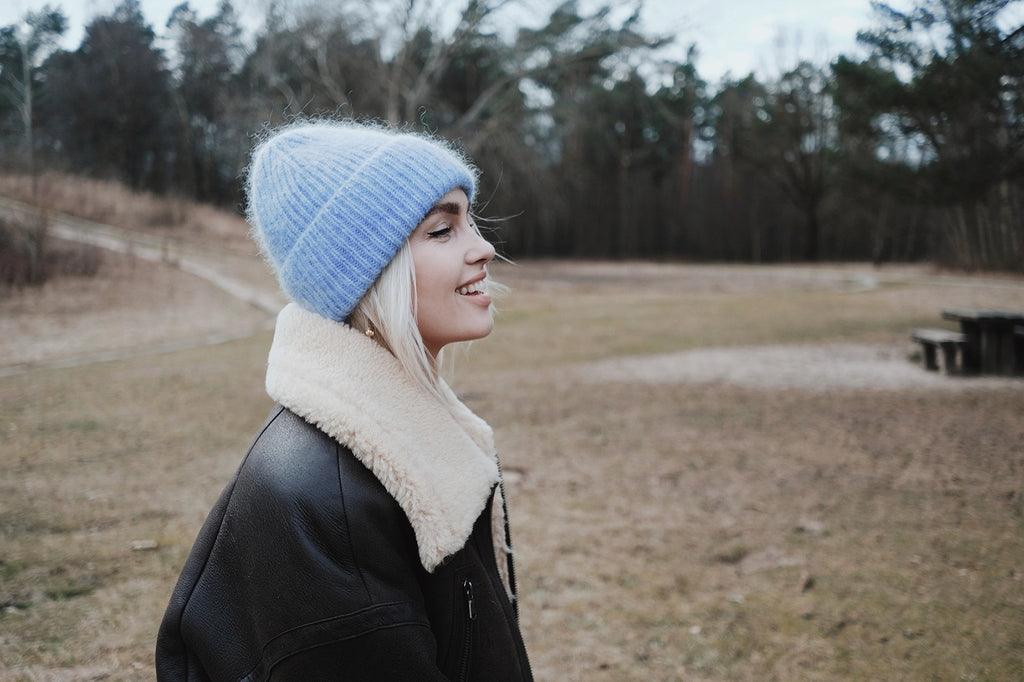 Linda Visser wearing a blue knit beanie and black coat with a shearling collar in an outdoor setting.