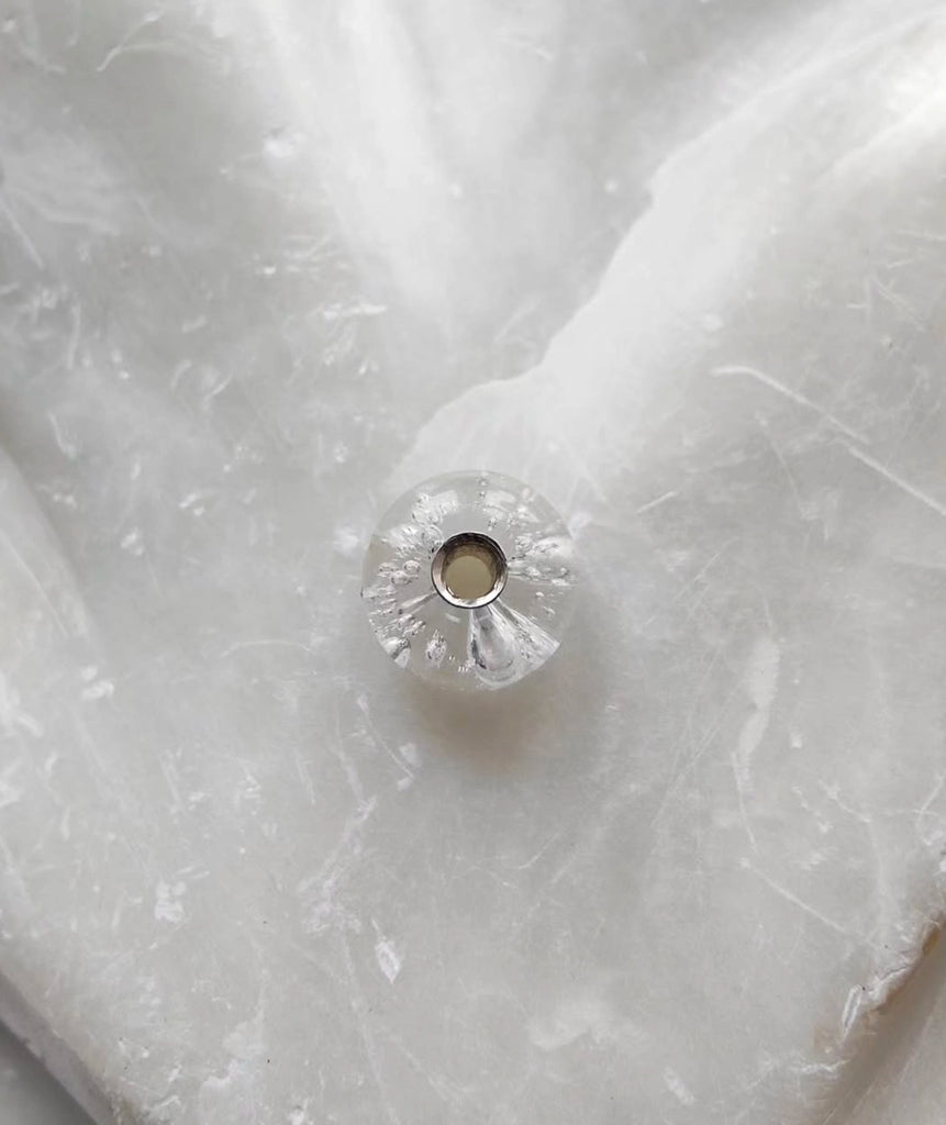 Close-up of a silver glass minimalist memorial pendant on a textured white fabric background.