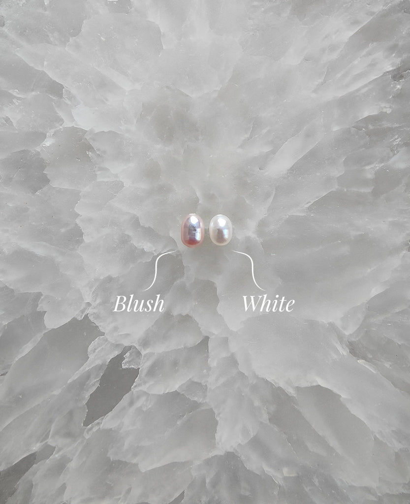 Two pearl earrings labeled 'Blush' and 'White' on a textured gray background.