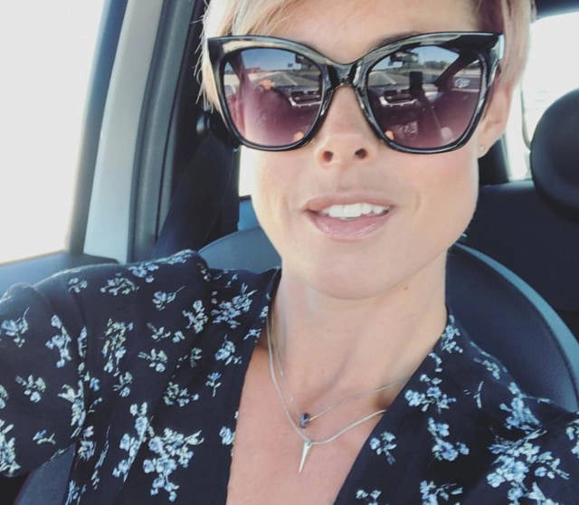 Woman wearing sunglasses and a floral blouse inside a vehicle. Wearing her memorial necklace made by The Seventh Sea.