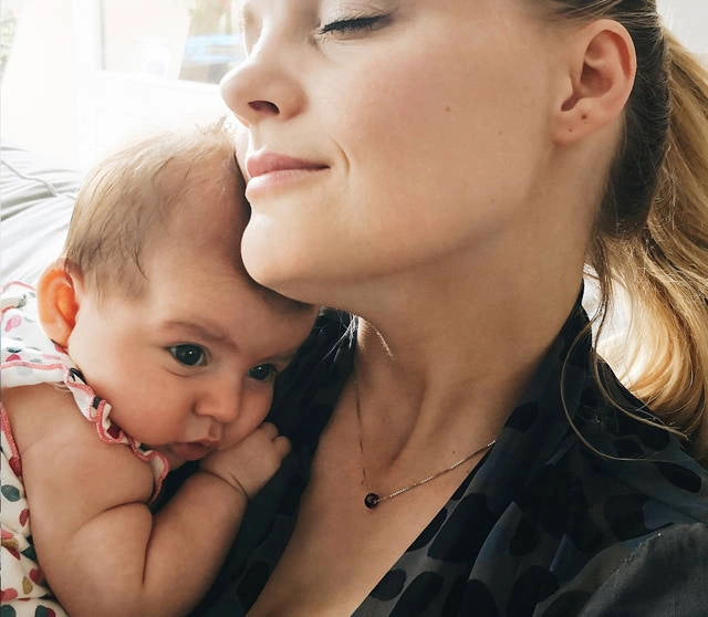 Woman holding a baby close to her face and wearing a memorial pendant to remember her brother.