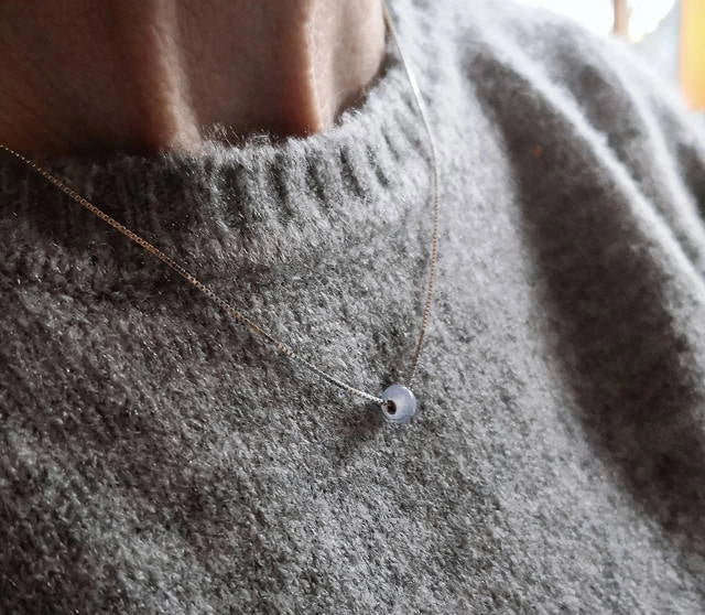 Necklace with a small memorial cremation pendant on a person wearing a gray sweater.