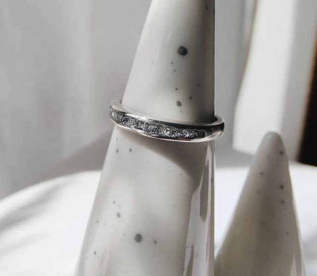Silver memorial ring with small stones on a white ceramic vase with black speckles.