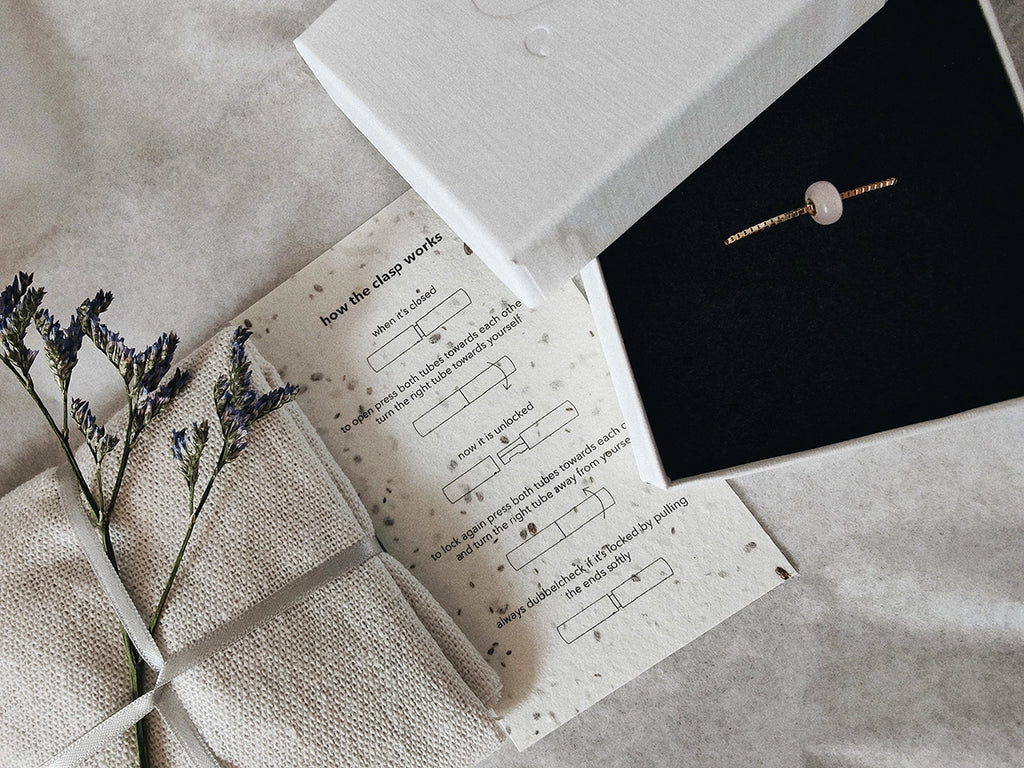 Jewelry box with a minimalist memorial pendant and instructions on a textured surface.