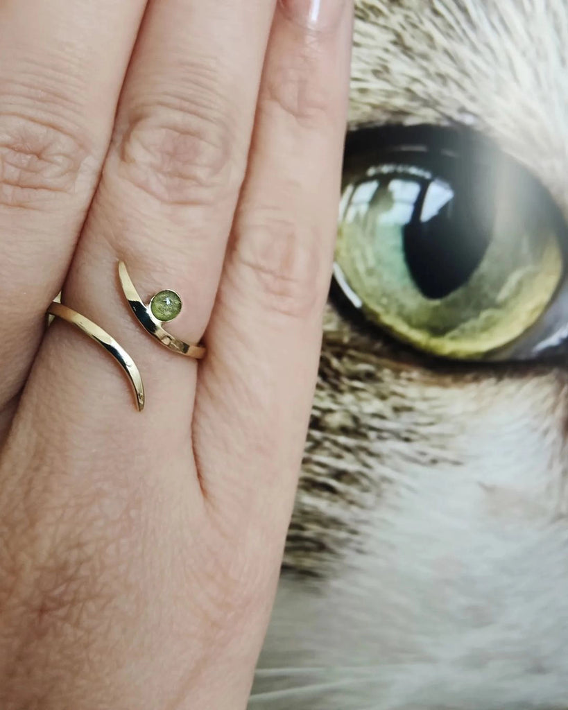 Gold cremation ring with a green gemstone on a finger next to a cat's eye.