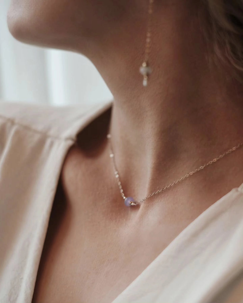 Necklace with small memorial pendant worn by a person, with a blurred background.